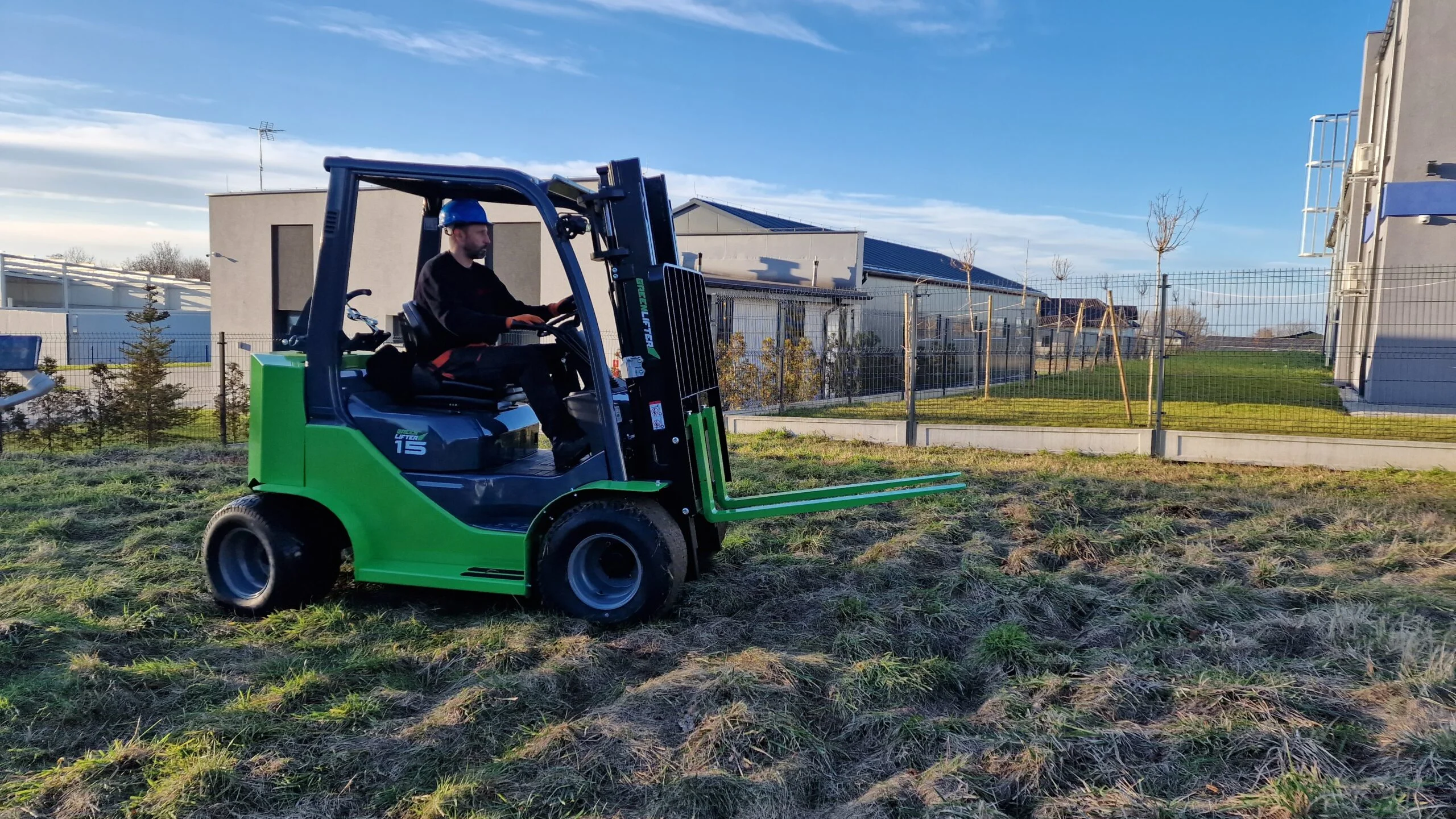 Man operating green forklift outdoors near industrial building