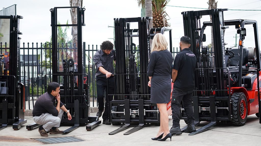 Employees inspecting new forklifts at outdoor equipment dealership