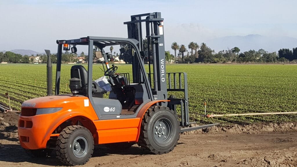 Orange forklift operating in green farmland field